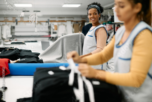 Young happy black woman using fabric roll while working at tailor's workshop.