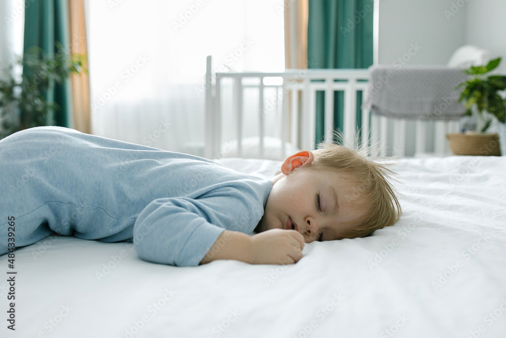 Cute little boy in blue sleepsuit sleeping in bed at home