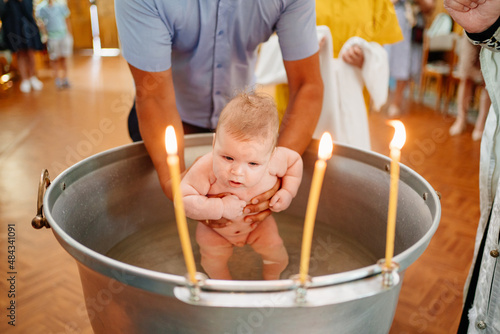 Obraz na plátně the baby boy is lowered into a font with holy water at baptism in the church