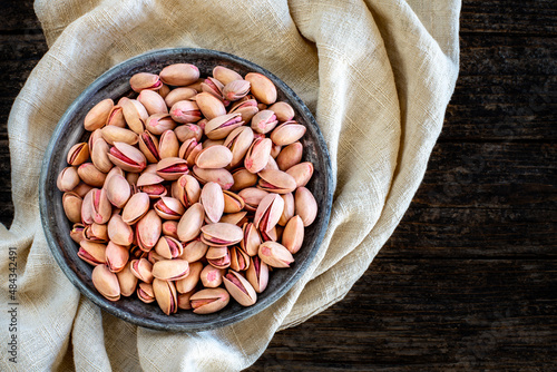 Many pistachios on the old rustic wooden bowl. Dried nuts concept.  photo