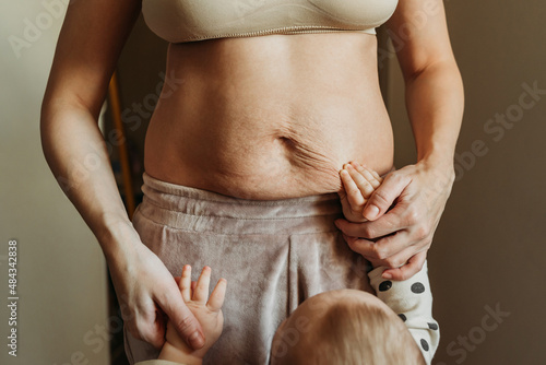 Little baby's hands on woman's belly full of stretch marks after pregnancy. photo
