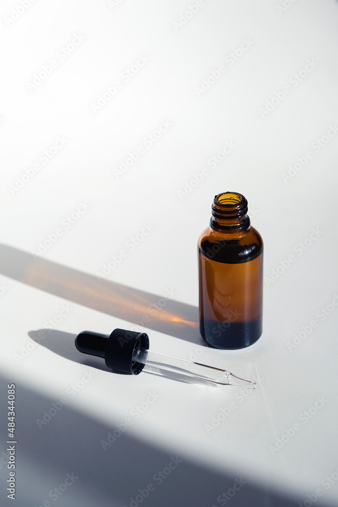 Open bottle with dropper pipette with serum or essential oil. White background with daylight. Skincare products , natural cosmetic. Beauty concept for face and body care