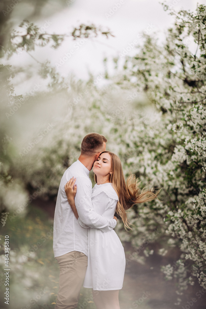 Happy family couple in love in a spring blooming apple orchard. Happy family enjoy each other while walking in the garden. The man holds the woman's hand. Family relationships Happy family couple in love in a spring blooming apple orchard. Happy family enjoy each other while walking in the garden. The man holds the woman's hand. Family relationships