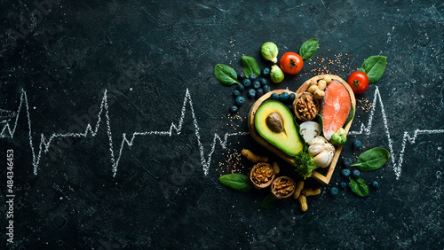 Food banner. Healthy foods low in carbohydrates. Food for heart health: salmon, avocados, blueberries, broccoli, nuts and mushrooms. On a black stone background. Top view. © Yaruniv-Studio