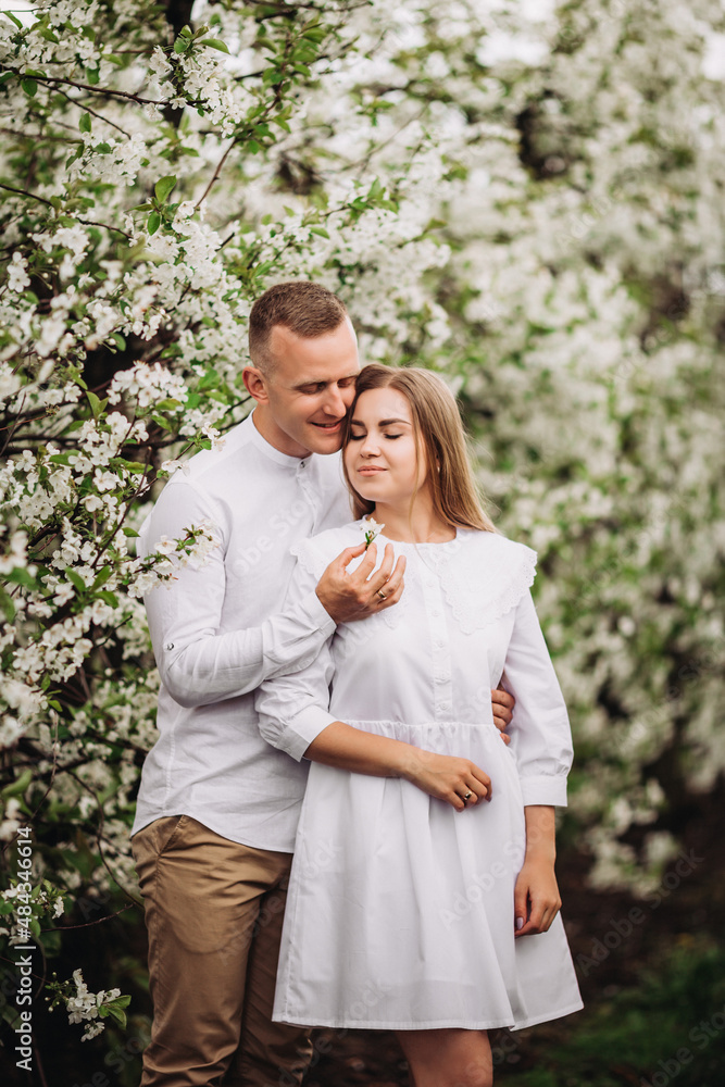 Happy family couple in love in a spring blooming apple orchard. Happy family enjoy each other while walking in the garden. The man holds the woman's hand. Family relationships Happy family couple in love in a spring blooming apple orchard. Happy family enjoy each other while walking in the garden. The man holds the woman's hand. Family relationships