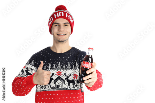 Odessa, Ukraine - 20 december 2021: Guy in Christmas sweater holds Coca-cola bottle, isolated on white background