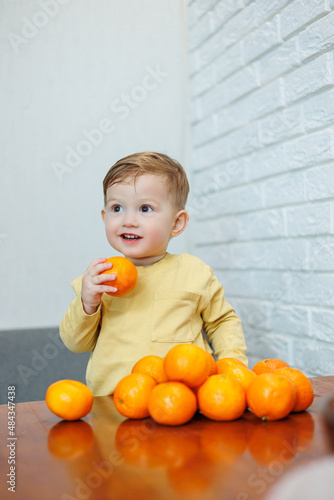 A little boy 2 years old is standing at a table with tangerines. Baby wants to sit down citrus fruits for the first time