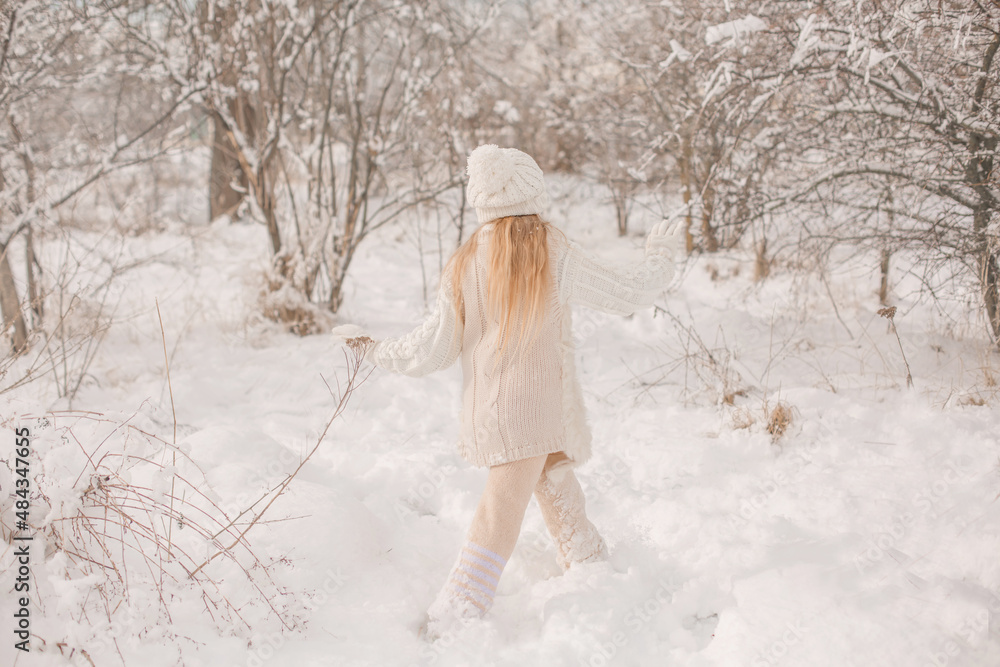 a happy little girl in a white knitted hat and sweater runs around a snowy park a happy little girl in a white knitted hat and sweater runs around a snowy park