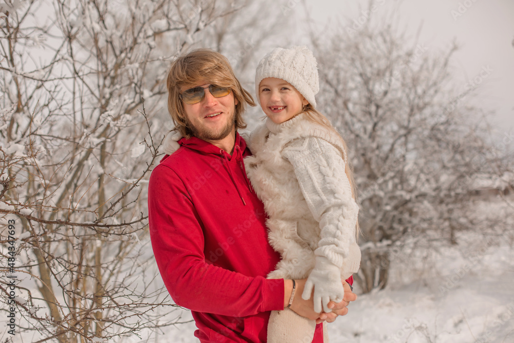 a little blonde girl in white knitted things a hat and a sweater is sitting on her father's arms in a red warm jacket a little blonde girl in white knitted things a hat and a sweater is sitting on her father's arms in a red warm jacket