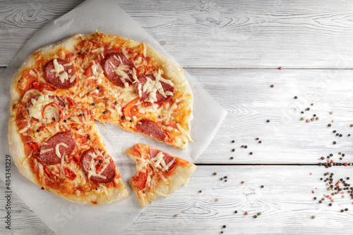 Hot pepperoni pizza on baking paper on white wooden background. Top view