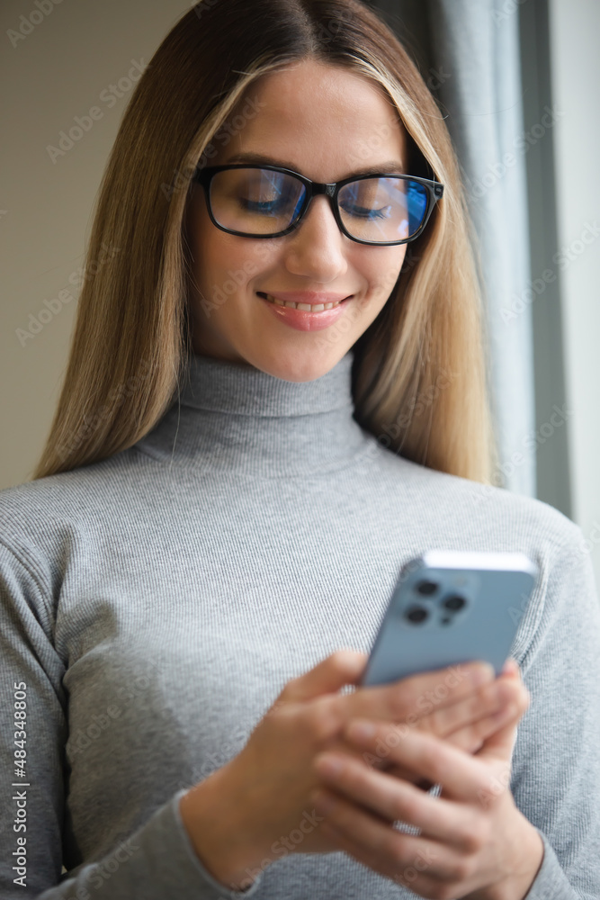 Happy blonde woman in glasses typing message online on modern mobile phone connected to internet. Cheerful white female using new smartphone for online communication and entertainment Happy blonde woman in glasses typing message online on modern mobile phone connected to internet. Cheerful white female using new smartphone for online communication and entertainment