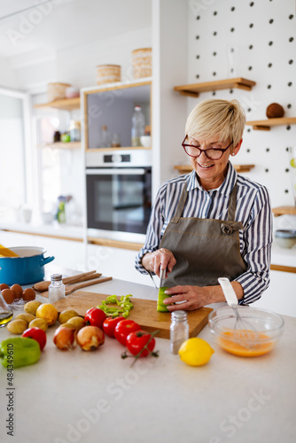 Beautiful mature woman in apron is preparing food and smiling while cooking in kitchen