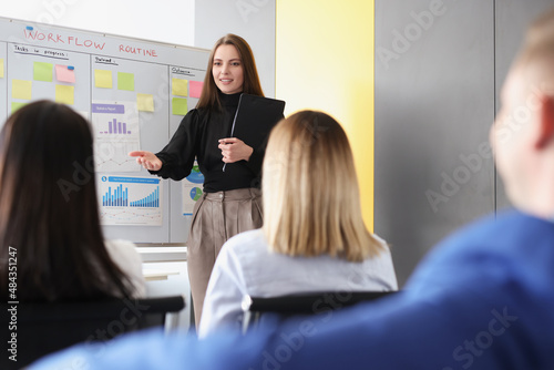 Woman coach explaining information to students in front of blackboard with graphs