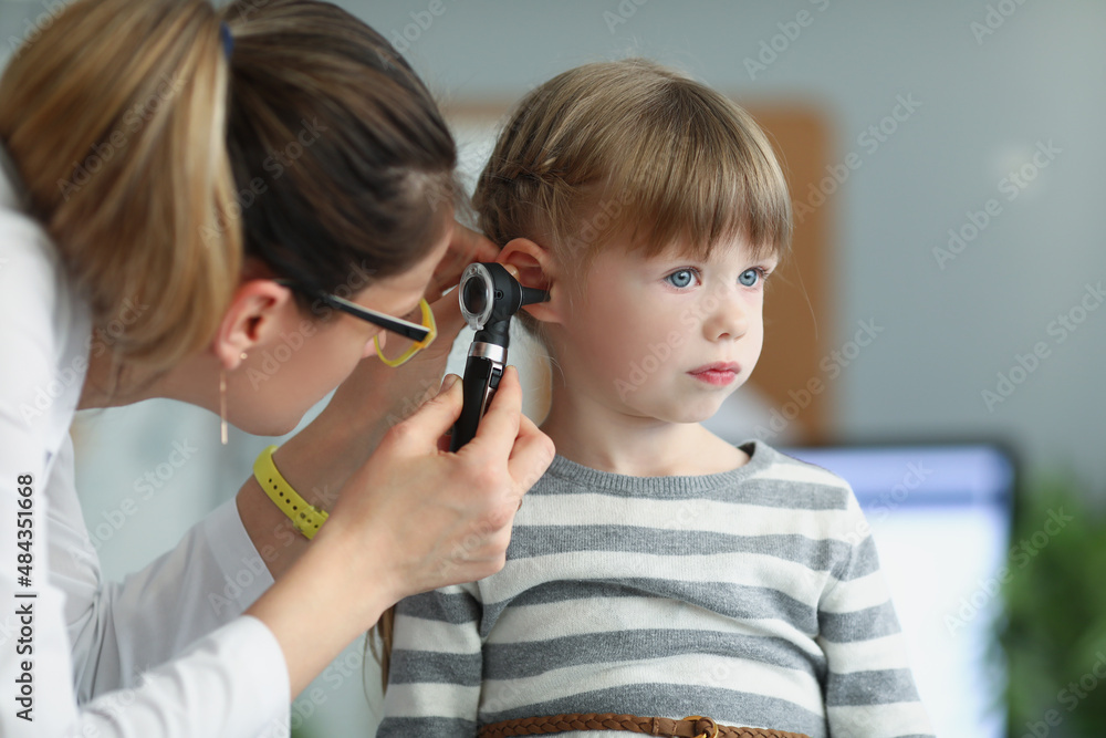 Female pediatrician looking at ear of little girl using otoscope in clinic