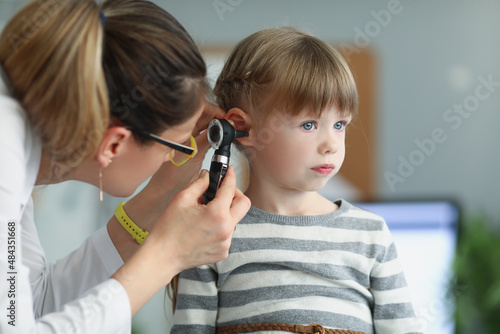 Obraz na płótnie Female pediatrician looking at ear of little girl using otoscope in clinic w salonie