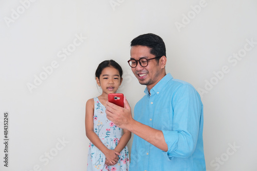 Asian father smiling happy while showing  mobile phone screen to his daughter photo