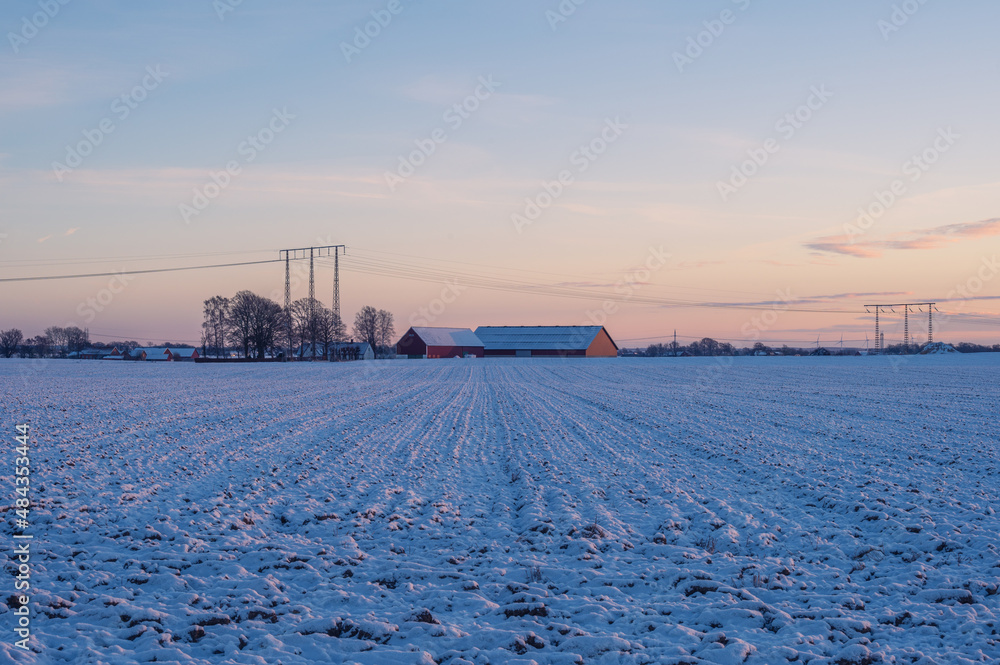 Barn in flat snow covered farm field in Skåne (Scania) Sweden during sunset