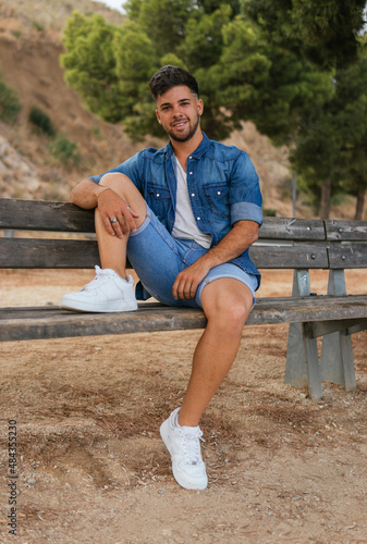 Handsome young man sitting on a bench of a viewpoint smiling and looking at the camera.