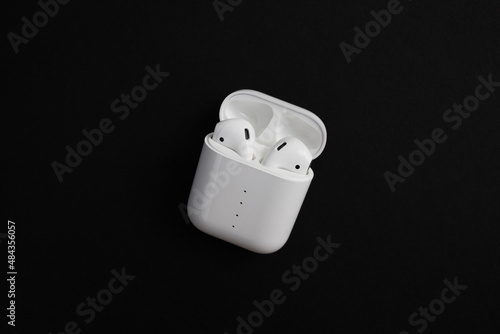Modern white wireless earbuds headphones lying in a charging case on black background.