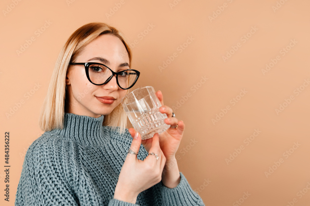 Beautiful girl is looking at the camera and holding a glass of water. The girl looks delightful and happy. Concept of photography Beautiful girl is looking at the camera and holding a glass of water. The girl looks delightful and happy. Concept of photography