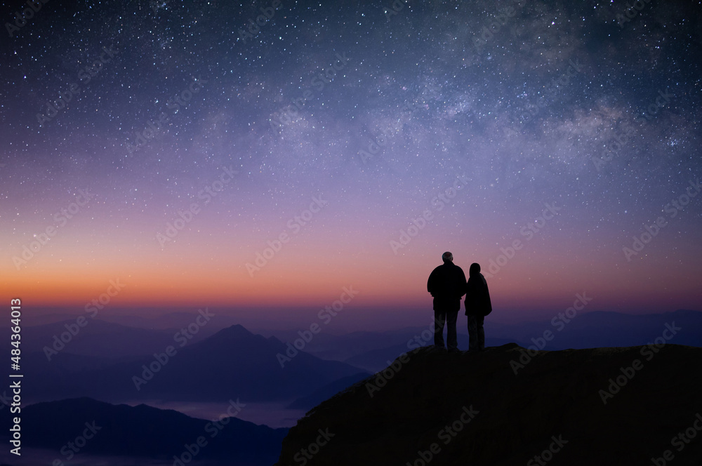 Silhouette of young couple of lovers watched the star, milky way, night sky on top of the mountain. They enjoyed traveling and was successful when he reached the summit.