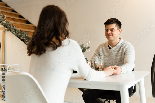romantic dinner at home in the kitchen on the background of christmas garlands.happy couple sit at the table and hold hands. pregnant girl.