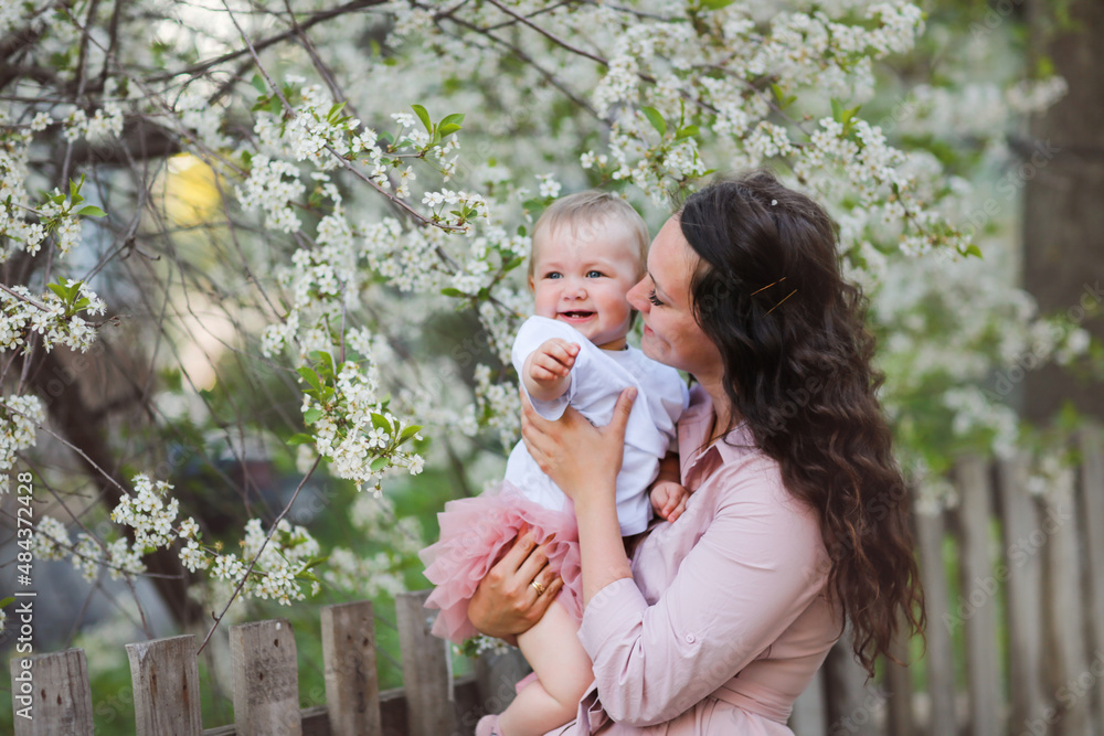 Lovely beautiful feminine mom with her daughter in her arms in spring with cherry blossoms. female natural beauty and beautiful wavy hair. Young European woman in a dress with a baby in a skirt. Lovely beautiful feminine mom with her daughter in her arms in spring with cherry blossoms. female natural beauty and beautiful wavy hair. Young European woman in a dress with a baby in a skirt.