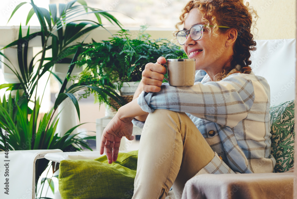 © simona - Adult woman smile sitting on the lounge chair and have relax time drinking cup of coffee or tea. Happy relaxed lifestyle for female people with eyeglasses
