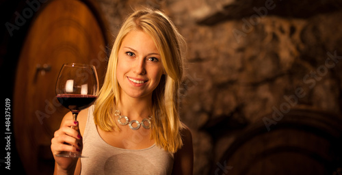 Фотография Beautiful young blond woman tasting red wine in a wine cellar