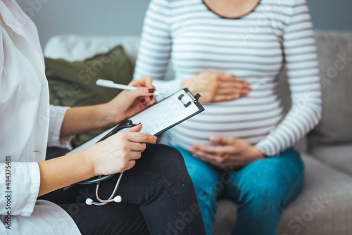 A female physician is meeting with a patient. The patient is a pregnant woman in her second trimester. The two women are having a pleasant conversation.  photo