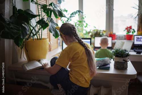 Distant education at home, two siblings doing homework together in one room. Elementary school kids during online class remotely, lockdown, new normal education. Soft focus on girl © Maria