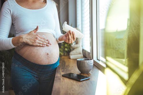 Belly of a pregnant woman applying moisturizer. Pregnant woman applying stretch mark removal lotion on her belly. Pregnancy, people and maternity concept photo