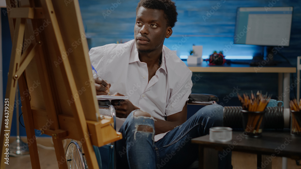 Invalid artist of african american ethnicity working on sketch for modern drawing in studio room at home. Black young person sitting in wheelchair while designing masterpiece for art project Invalid artist of african american ethnicity working on sketch for modern drawing in studio room at home. Black young person sitting in wheelchair while designing masterpiece for art project