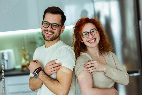 Happy young couple showing their arms after covid 19 vaccine with adhesive plasters.
