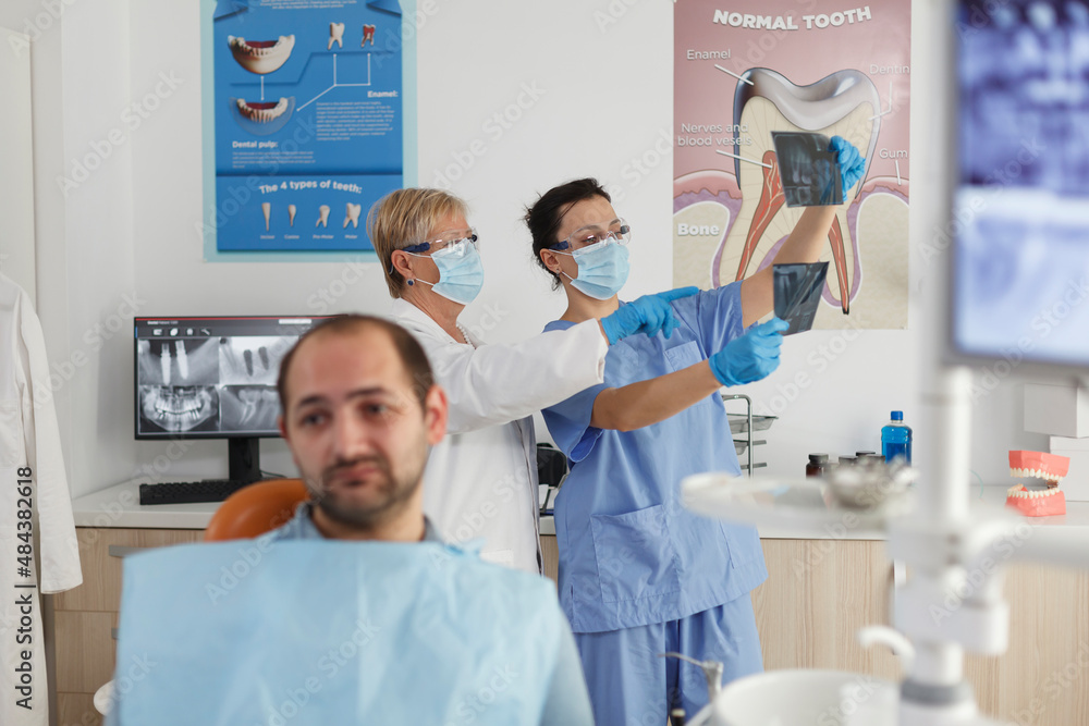 Obraz premium Portrait of patient with toothache waiting for medical expertise during stomatological examination in dentistry office room. In background medical team analyzing teeth radiography. Medicine service
