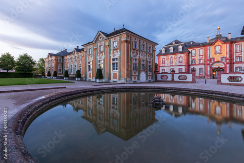 Bruchsal castle at blue hour with a fountain in the foreground and reflection in the water. Dramatic sky. photo