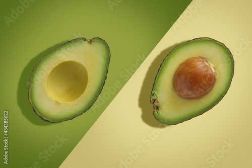 Two avocado halves diagonally on a green and beige background.