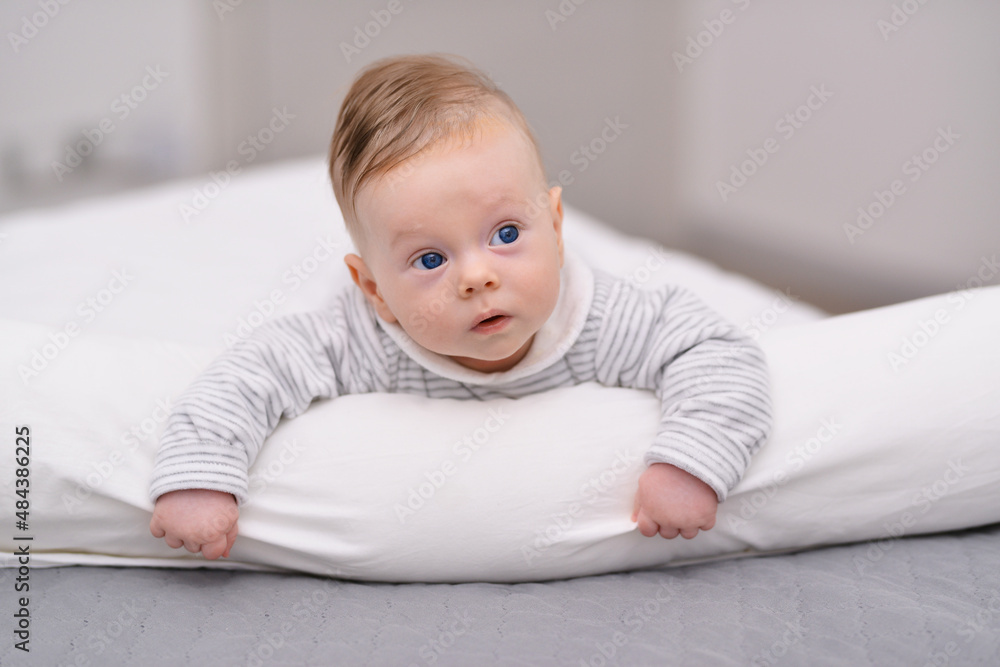 Cute baby lying on her stomach on soft blanket and looks away with surprised.