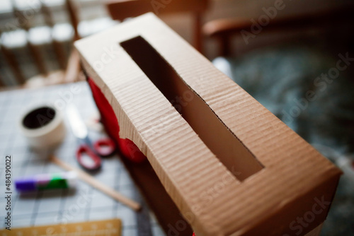 A child plays a homemade cardboard theater at home in a real interior, creative development of children, a happy childhood. photo