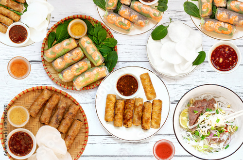 Close-up of Vietnamese spring rolls with chicken, tiger prawns, Pho bo, Vietnamese soup with noodles and beef, fresh herbs, rice chips on a wooden board. Sesame sauce. A Variety Of Vietnamese Food. 