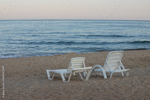 Two sunbeds on a sandy calm beach with turquoise sea water and white sand