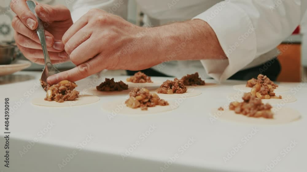 Chef puts meat paste onto dumplings dough on kitchen table. Close up. Chef puts meat paste onto dumplings dough on kitchen table. Close up.