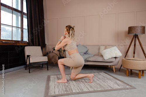 Back view of young healthy woman in sport clothing doing deep squats during domestic workout. Pretty blonde leading healthy and active lifestyle for keeping fit.