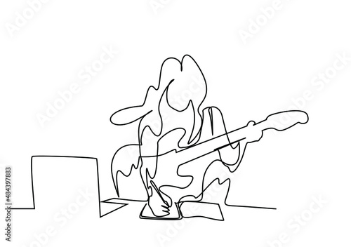 female singer artist holding guitar and laptop in front of her composing and taking notes