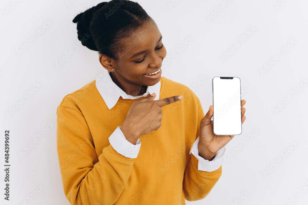 Fashion mobile phone. Smiling african american woman holding latest thin smartphone with blank screen and pointing at it. Fashion mobile phone. Smiling african american woman holding latest thin smartphone with blank screen and pointing at it.