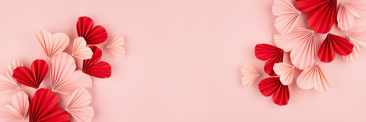 Holiday Valentine day banner for website with flow of flying pink and red paper folded ribbed hearts on soft light pink background as festive backdrop, top view, copy space.