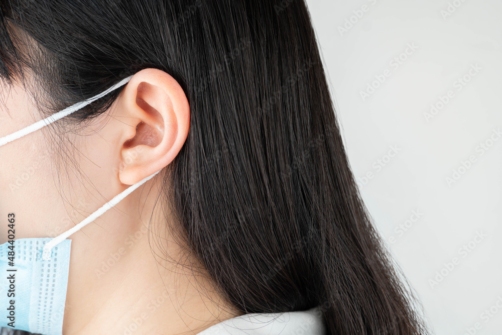 Backs of woman ears with medical face mask. Mask wearing may lead to
