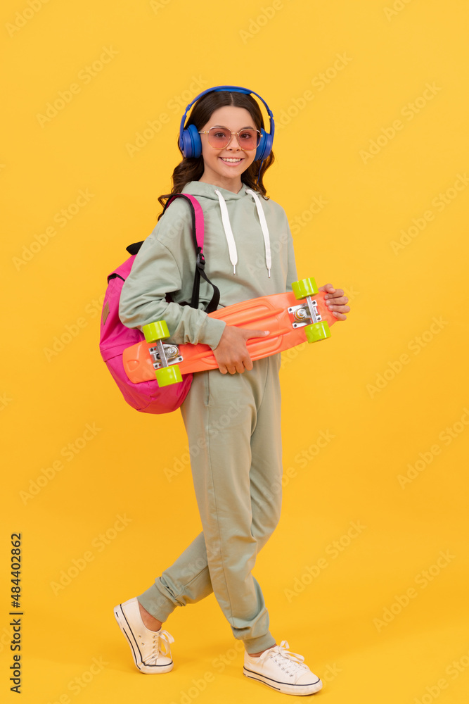 Happy kid in activewear holding penny board yellow background, skateboarding Happy kid in activewear holding penny board yellow background, skateboarding