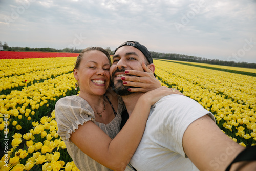Caucasian couple taking a selfie in a flower field full of yellow and red tulips in the Netherlands