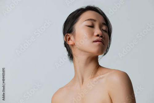 Cropped sudio portrait of tender young woman posing with closed eyes isolated over gray background
